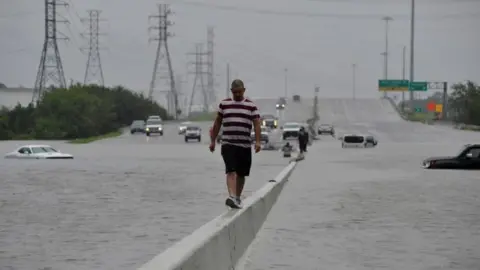 Reuters A stranded motorist escapes floodwaters on Interstate 225 after Hurricane Harvey inundated the Texas Gulf coast (27 August 2017)