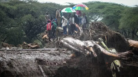 AFP People stand on debris blocking a highway on a bridge after the River Muruny burst its banks in West Poko, Kenya - November 2019