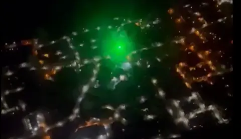 A green laser shining amongst others lights on the ground