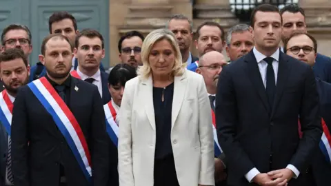 Getty Images Marine Le Pen (centre) and her far-right National Rally party holding a minute's silence outside the French parliament for Lola