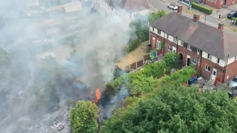 Christopher Furlong In this aerial view Firefighters contain a wildfire that encroached on nearby homes in the Shiregreen area of Sheffield on July 20, 2022 in Sheffield, England.