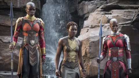 Marvel Studios Movie still of three women warriors of Wakanda in armour holding spears.