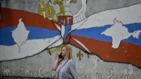 AFP via Getty Images A woman walks past a mural reading "Kosovo is Serbia and Crimea is Russia" in the Serb majority north of Mitrovica, Kosovo