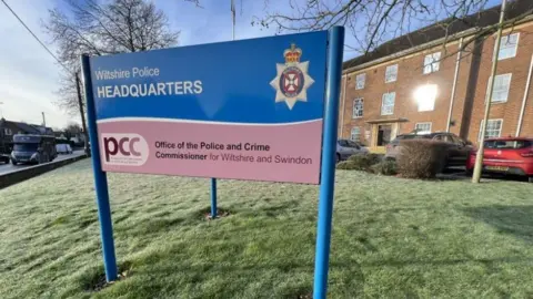 BBC The Wiltshire Police sign in front of their headquarters made from red brick in Devizes
