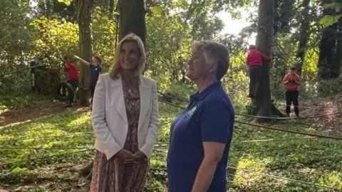 BBC The Duchess of Edinburgh with Dr Celia Grummit. They are stood in the woods, with some school children in the background