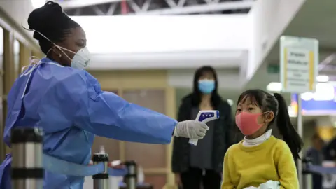 EPA A Kenyan health worker (L) screens a passenger wearing face mask after they arrived from China, at Jomo Kenyatta International Airport in Nairobi, Kenya, 29 January 2020