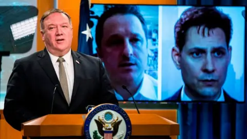 AFP via Getty Images Michael Spavor and Michael Kovrig are shown on a video monitor as US Secretary of State Mike Pompeo, speaks during a news conference in July