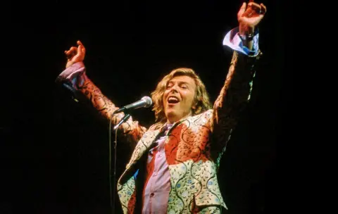 Jim Dyson / Getty Images David Bowie holds his hands into the air