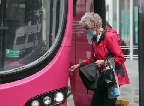 Pacemaker An elderly woman wearing a mask gets on to a bus