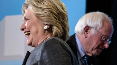 Getty Images Hillary Clinton and Bernie Sanders face different directions at a 2016 campaign event.