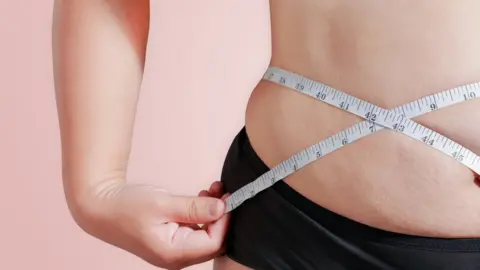 Getty Images Close up of female measuring her waist with a tape measure.