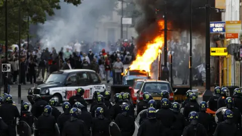 Reuters Police officers in riot gear block a road near a burning car on a street in Hackney, east London August 8, 2011