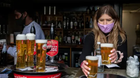 Getty Images woman serves pints behind the bar