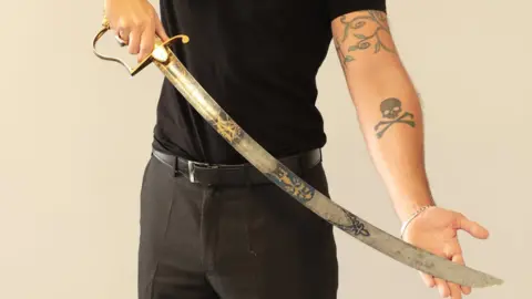 Duke's Auction House Man with tattoos holding sword