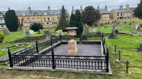 Huntingdon Town Council Grave surrounded by newly-painted black railings and dominated by an urn that has lost its cracks