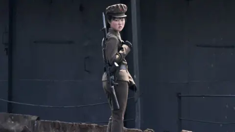 Reuters North Korean female officer in green uniform and gun looks at camera