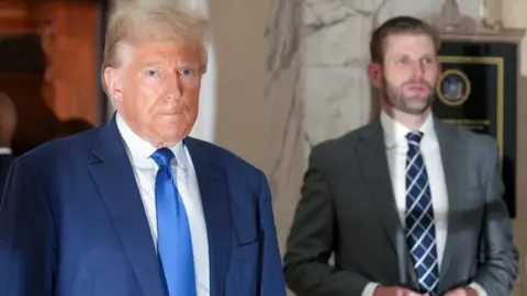 Reuters Donald Trump in blue suit with blue tie, Eric Trump in grey suit.