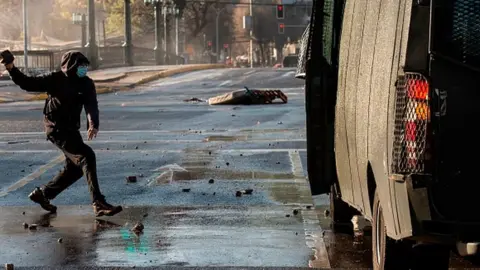 Getty Images A demonstrator wearing a face mask throws a stone at a riot police vehicle during clashes following a protest against Chilean President Sebastian Pinera's government in Santiago