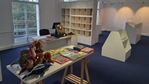 Swindon Borough Council Image inside the new museum space. Empty shelves and a table full of books and stuffed toys can be seen.