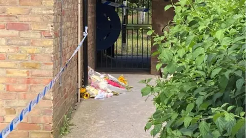 Nadia Gyane/BBC Police tape at the side of the building where soft toys and flowers have been left.