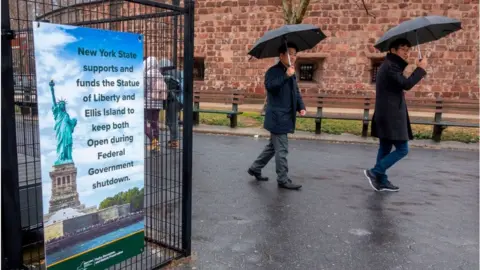 Getty Images People walk past a sign announcing that New York funds are keeping the Statue of Liberty and Ellis Island open for visitors on January 5, 2019, in New York