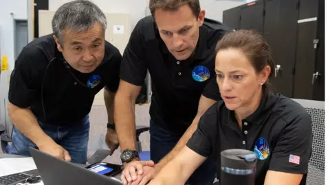 NASA Nicole Mann, Josh Cassada and Koichi Wakata gather around a laptop during training