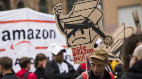 Getty Images People hold banners during a demonstration attended from Amazon-Workers, trade union members and left activits under the motto 'Make Amazon Pay' in Berlin, Germany on April 24, 2018.