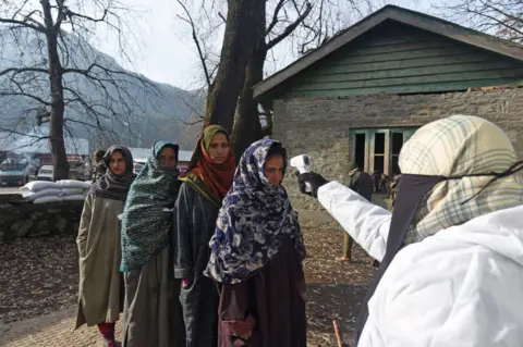 Getty Images A health worker thermal screens voters arriving at a polling station to cast their vote.