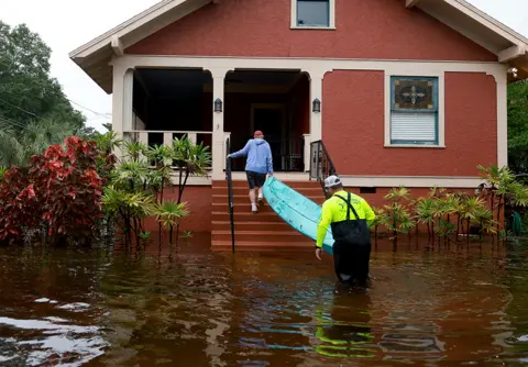 Joe Raedle / Getty Images People carry a kayak onto his porch through the flooded streets caused by Hurricane Idalia passing offshore on August 30, 2023 in Tarpon Springs, Florida