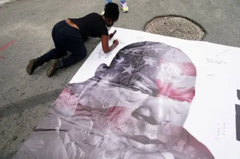ELIJAH NOUVELAGE/Reuters A woman signs a picture of late US Congressman John Lewis