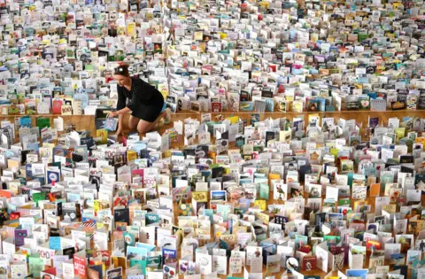 Shaun Botterill/Getty Images Mandy Alison adds to the thousands of birthday cards sent to Captain Tom Moore for his 100th birthday on 30 April, are pictured displayed in the Hall of Bedford School.