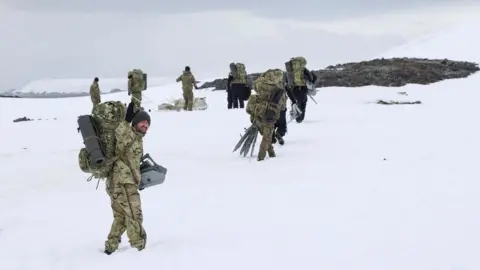 Royal Navy LET(WE) Chapman waves as sailors from HMS Protector prepare to set up camp for the night