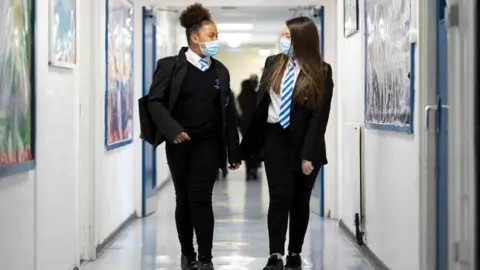 Getty Images Two schoolgirls talking in a school corridor while wearing face masks