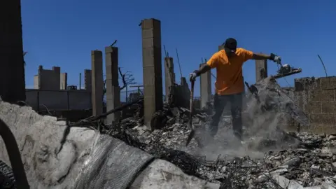 Reuters A man with a shovel stands on a large pile of debris in the ruins of a house