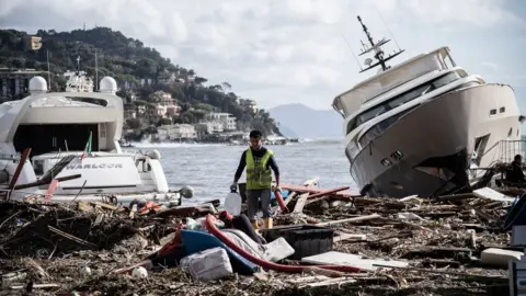 Getty Images A man walks through garbage between two yachts after a storm hit the harbour and destroyed a part of the dam during the last night on October 30, 2018