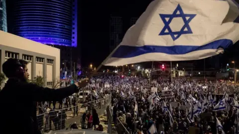 Getty Images A protester waves the Israeli flag during a massive protest against the government's judicial overhaul plan on 11 March 2023 in Tel Aviv