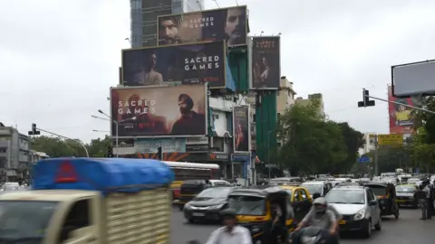 Getty Images This photo taken on July 4, 2018 shows Indian commuters travelling past large billboards for 'Sacred Games', the upcoming Indian series on Netflix, in Mumbai.