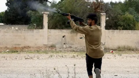 Getty Images A fighter loyal to the Libyan internationally-recognised Government of National Accord (GNA) fires a Kalashnikov rifle during clashes against forces loyal to strongman Khalifa Haftar, on May 21, 2019 in the Salah al-Din area south of the Libyan capital Tripoli. - Despite a UN embargo, weapons are still flowing into Libya where an assault on the capital by Haftar threatens to escalate into a proxy war between regional powers. Haftar, whose self-styled Libyan National Army (LNA) is allied with an administration in eastern Libya, is supported especially by Egypt and the United Arab Emirates (UAE).