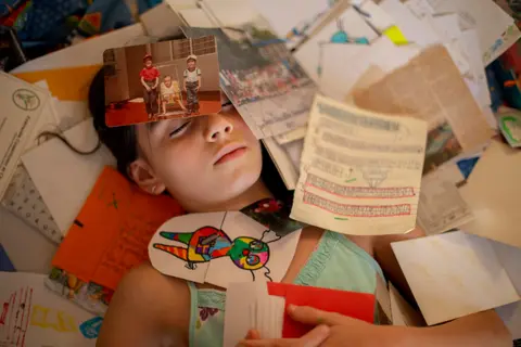 Priscilla Mora Flores / Unicef A girl lies on the floor covered with photos and papers