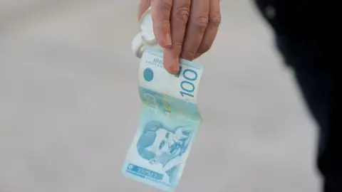 Reuters A man holds a dinar currency and a coffee cup in Mitrovica, Kosovo, February 1, 2024