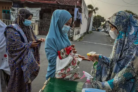 Rizqullah Hamiid / Getty Images A woman sprays hand sanitizer on to the hand of another woman before Eid al-Fitr prayers in Yogyakarta, Indonesia