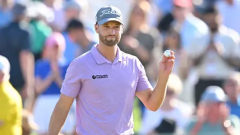 Wyndham Clark holds up his ball