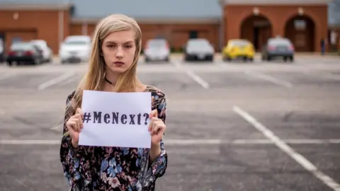 Kimberley Wheeler Mackenzie Jones holds up a sign in a car park saying #MeNext