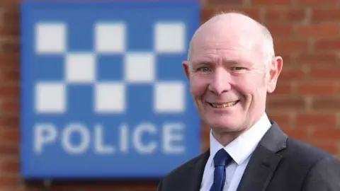 Conservative Party Darryl Preston in front of police sign