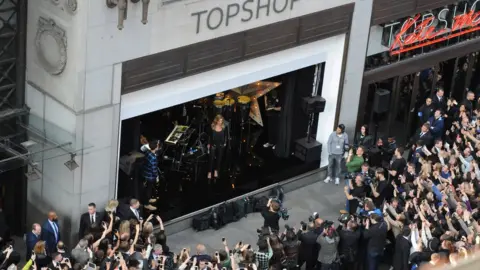 Getty Images Kate Moss stands in a window of Topshop in 2014