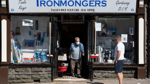 Getty Images An independent shop keeper serving a customer from the door of his shop