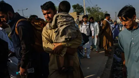 Getty Images Afghans make their way the road to the military entrance of the airport for evacuations, in Kabul, Afghanistan