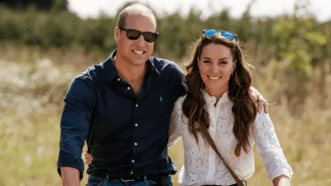 Kensington Palace/PA William is wearing sunglasses, jeans and a blue shirt and Kate is wearing a white shirt and jeans. A pair of sunglasses rests on Kate's head.