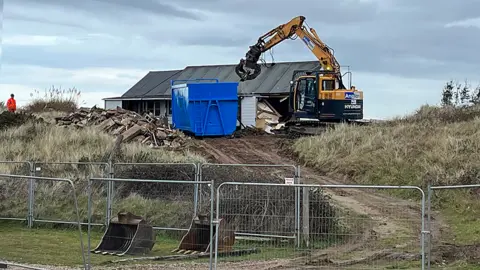 Shaun Whitmore/BBC Claw digger demolishes wooden home on The Marrams in Hemsby, Norfolk