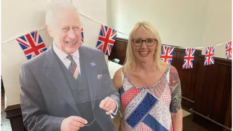 Storehouse Project Manager, Jill Neighbour, stood next to a cardboard cut out of King Charles III who is laughing and points in a kilt and blazer